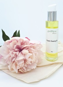 Guiltless Skin's cleaning oil, which is pal yellow in colour, standing on an organic cloth with a pink flower on the left.