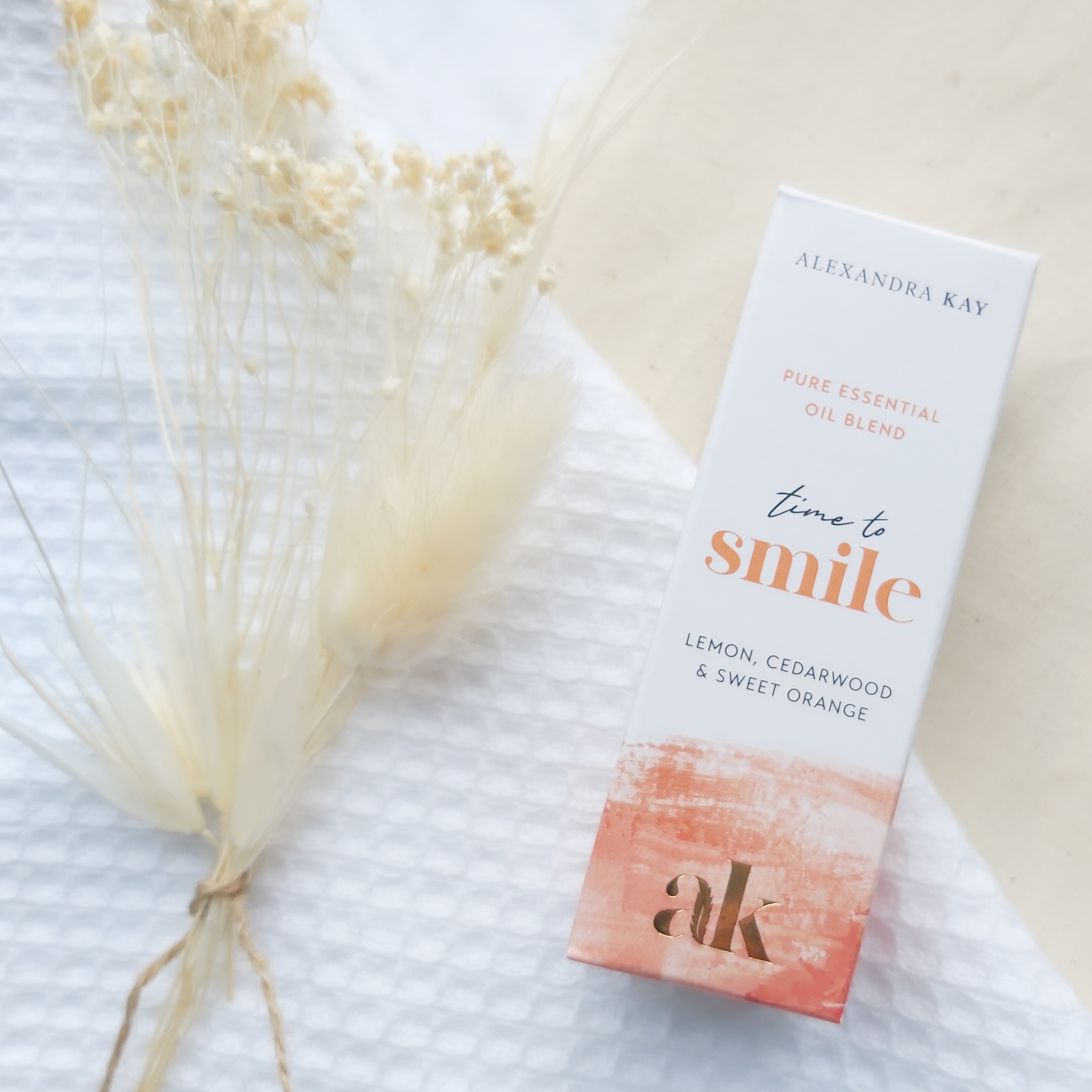 Green People's Alexandra Kay Wellness Time to Smile Essential Oil Box on a white flannel and linen cloth with dried flowers. Review by Beauty Folio