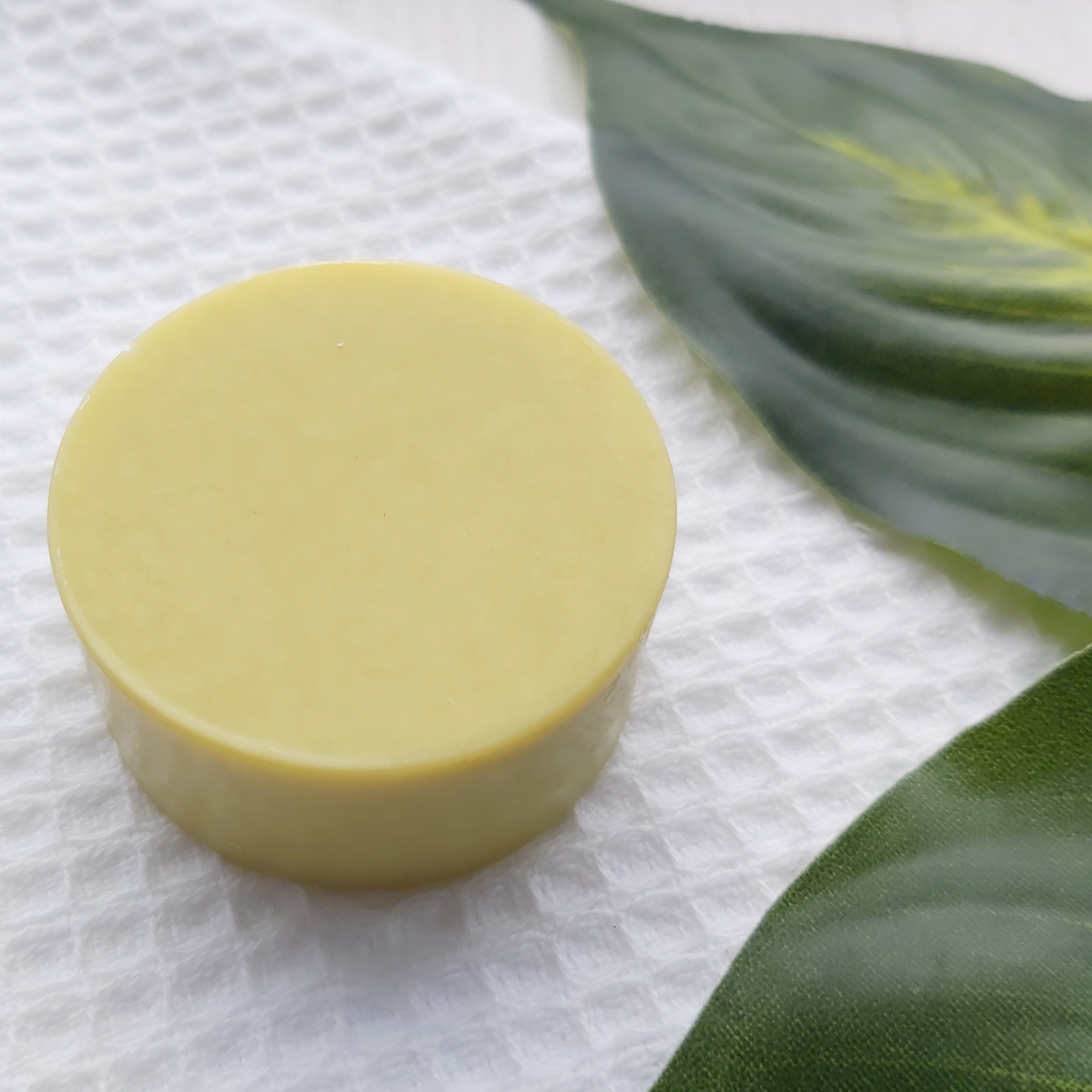 Nudge Boutique Cocoa & Avocado Oil to Milk Cleansing Bar sat on a waffle flannel and green leaves to the side - Review by Beauty Folio