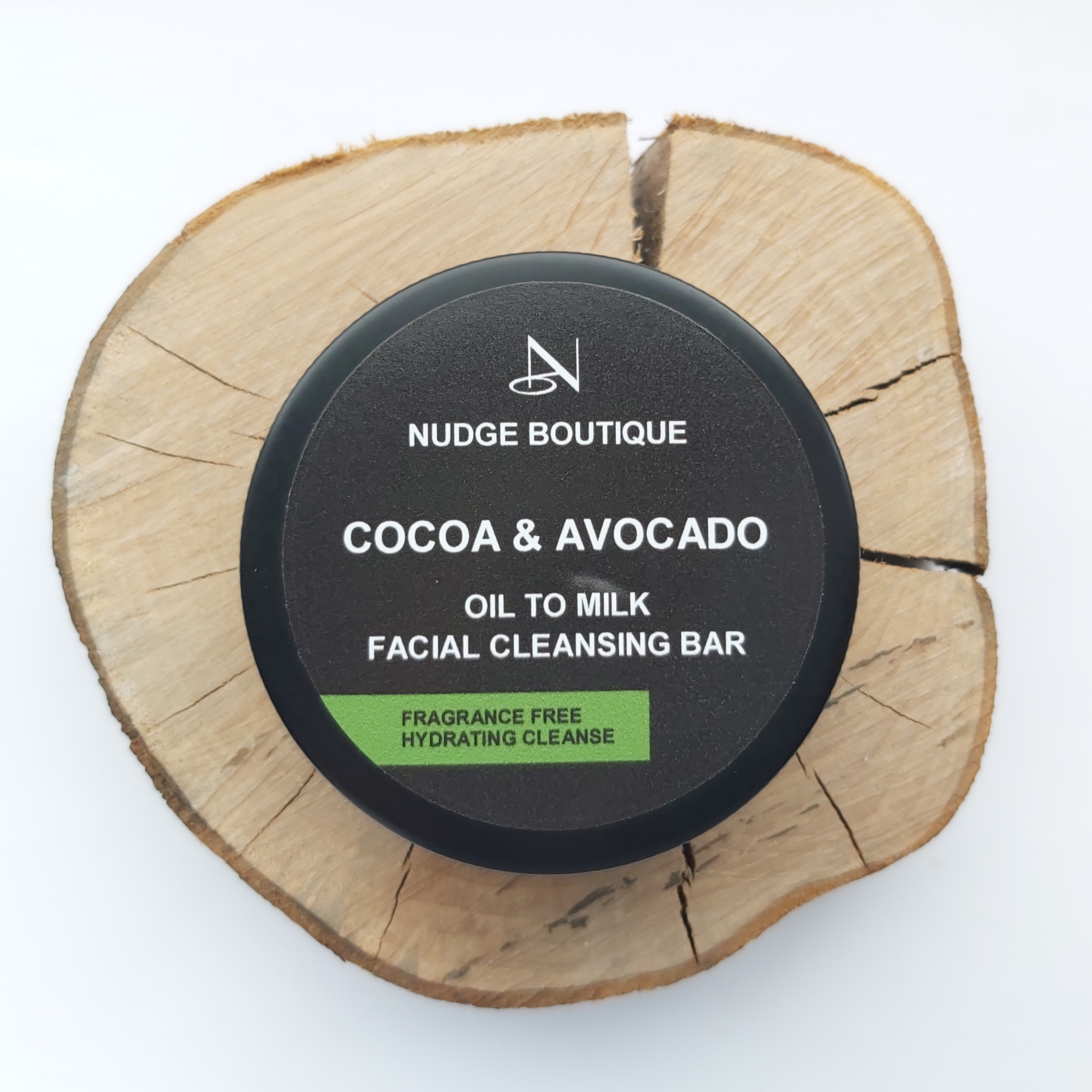 Nudge Boutique Cocoa & Avocado Oil to Milk Cleansing Bar in a black aluminium tin on a wooden slice and white background - Review by Beauty Folio