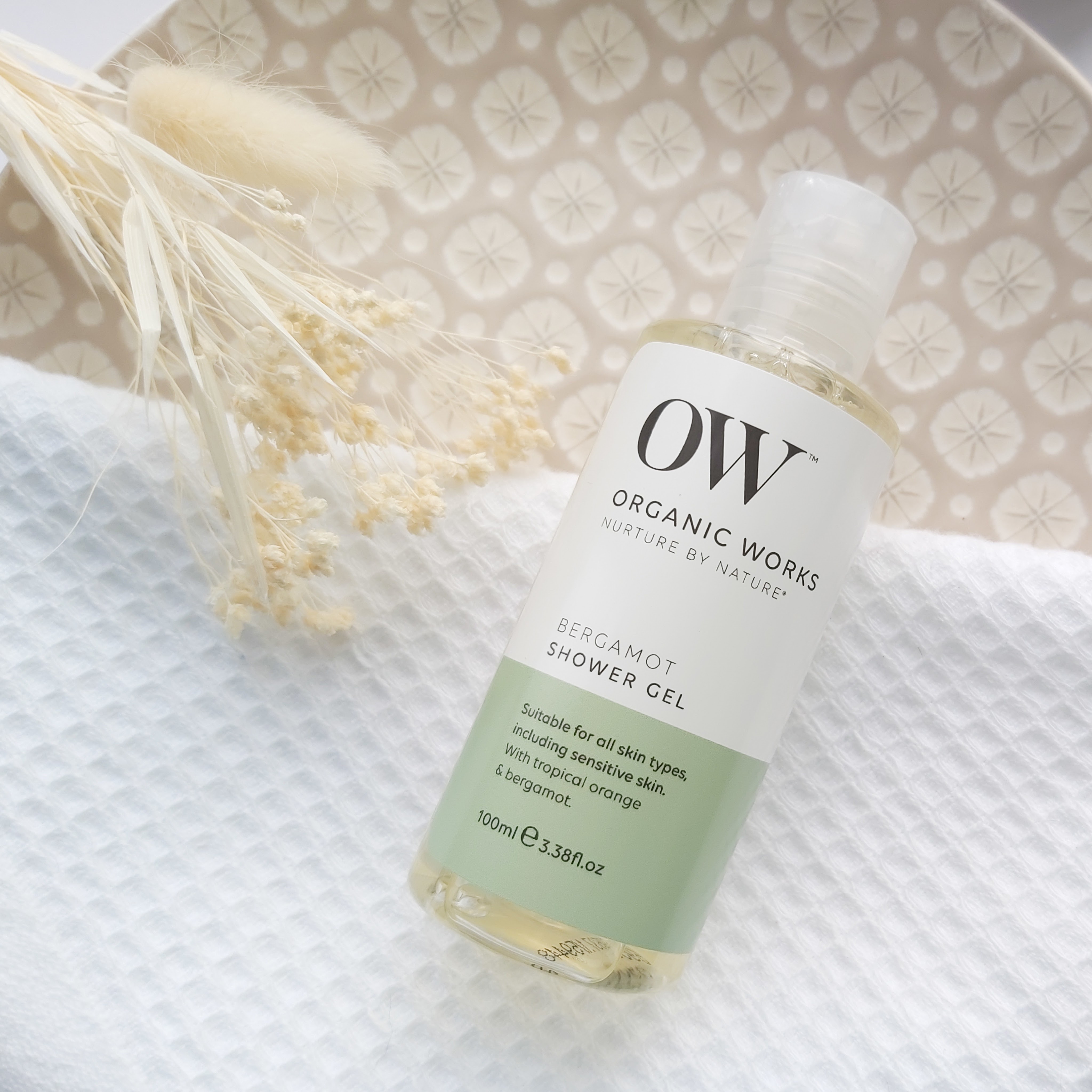 Organic Works bergamot shower gel featured in The Natural Beauty Box May 2021 on a patterned plate, waffle white towel and natural foliage - Review by Beauty Folio