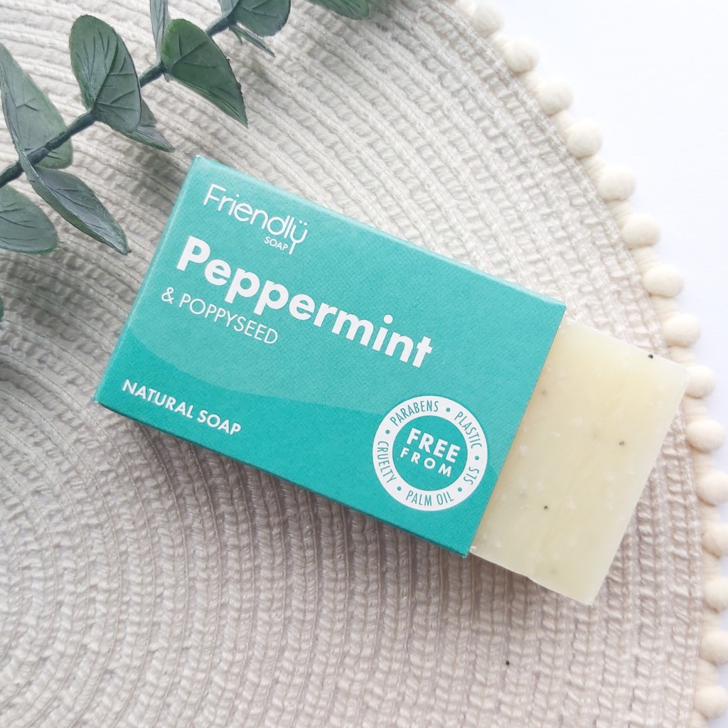 A bar of peppermint and poppy seed Friendly Soap  sticking out of the box laid on a beige place mat with pom pom edge and a eucalyptus stem. A Plastic Free Green Beauty Guide by Beauty Folio highlighting plastic pollution and plastic free beauty from Lovethical. 
