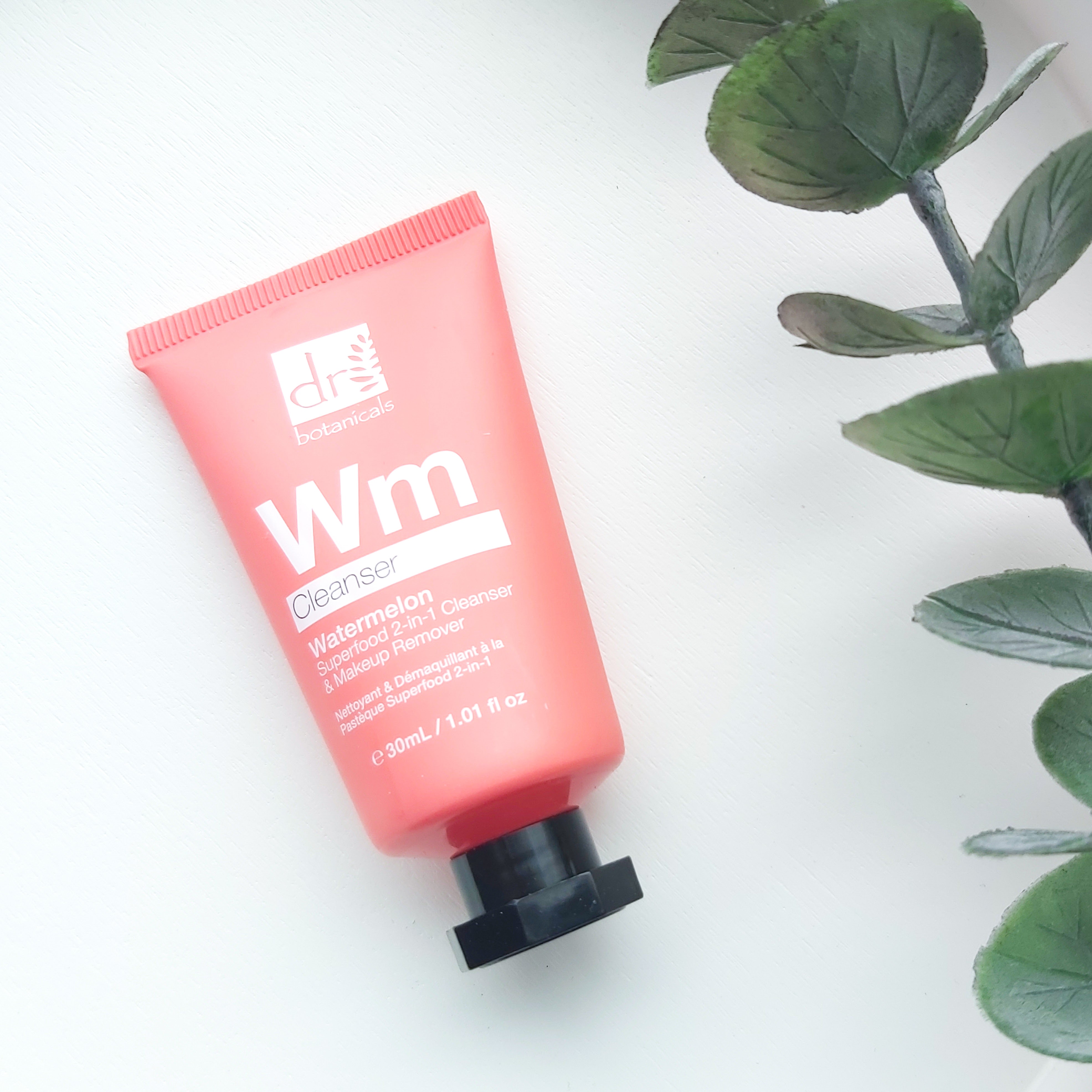 A pink tube of Dr Botanicals Watermelon Cleanser and Make-Up Remover sits on a white, wooden round tray with a eucalyptus stem to the side - Freedm Street Subscription Beauty Box review by Beauty Folio