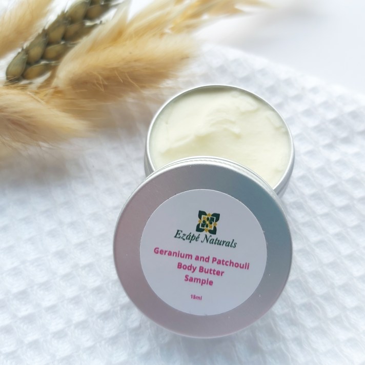 A 15ml tin of Ezape Naturals Geranium and Patchouli Body Butter open on a white waffle flannel and spring of neutral dried flowers in the background. Review by Beauty Folio.