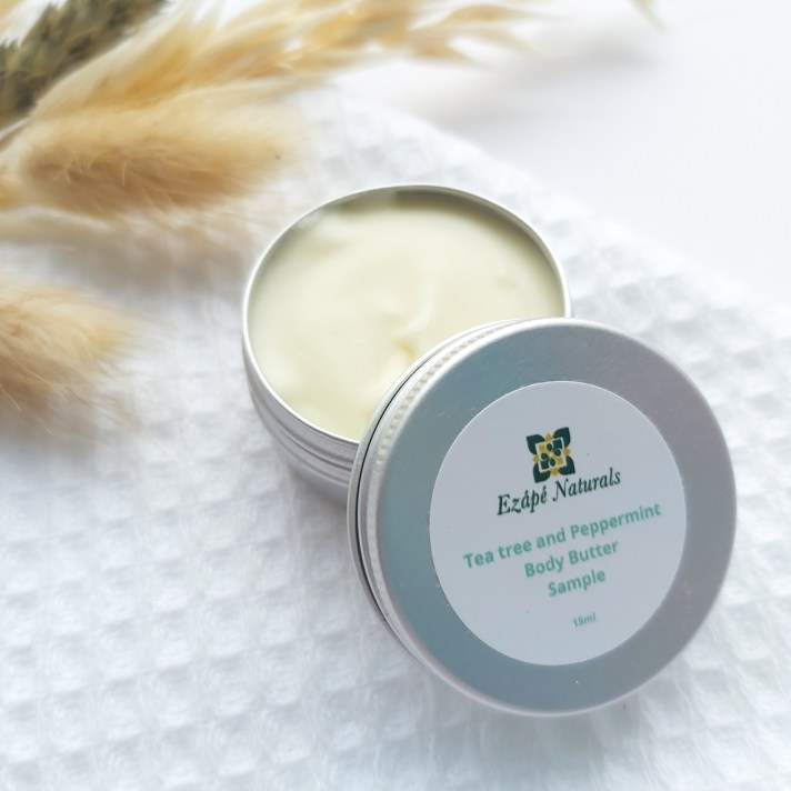 A 15ml tin of Ezape Naturals Tea Tree and Peppermint Body Butter open on a white waffle flannel and spring of neutral dried flowers in the background. Review by Beauty Folio.