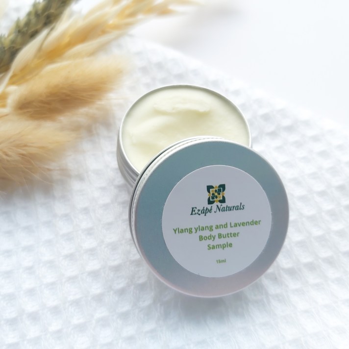 A 15ml tin of Ezape Naturals Ylang Ylang and Lavender Body Butter open on a white waffle flannel and spring of neutral dried flowers in the background. Review by Beauty Folio.