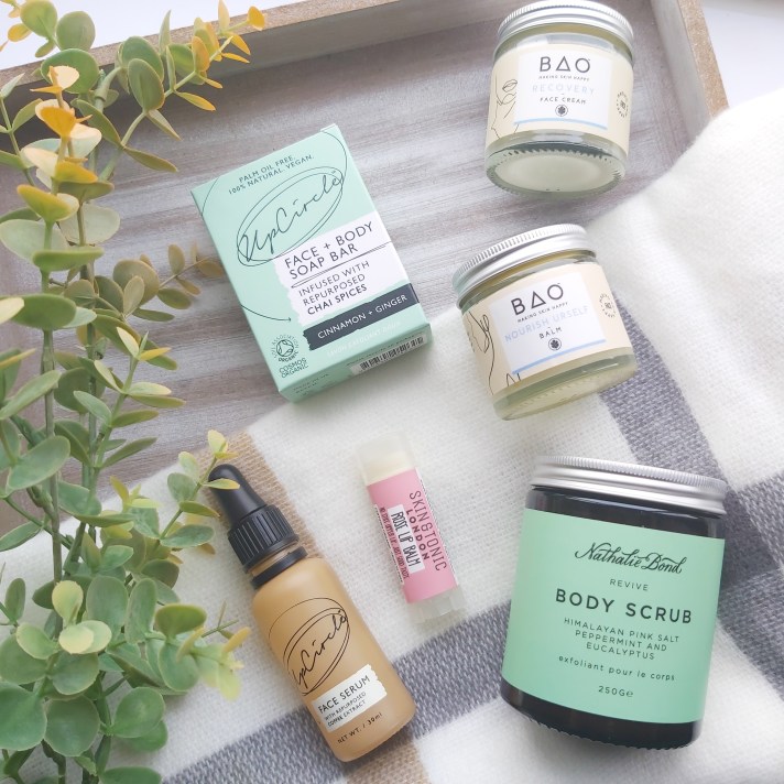 All top picks on a check blanket with green eucalyptus foliage and wooden tray. Green Beauty Guide - Kind Origins Review by Beauty Folio.