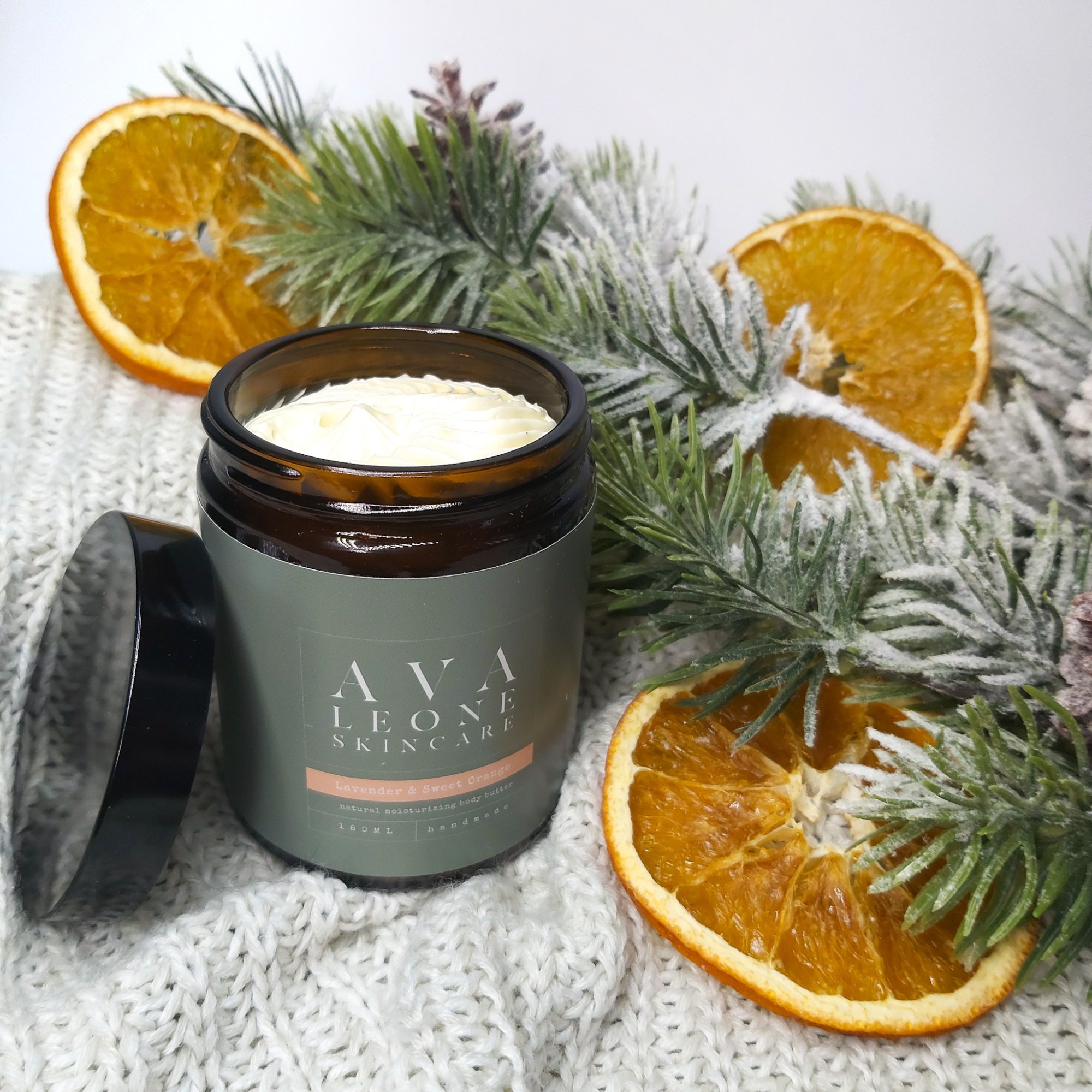 Avaleone Lavender & Orange Body Butter in an open jar, sat on a beige knitted blanket with Christmas foliage and orange slices. Natural Beauty Christmas Gift Guide by Beauty Folio.