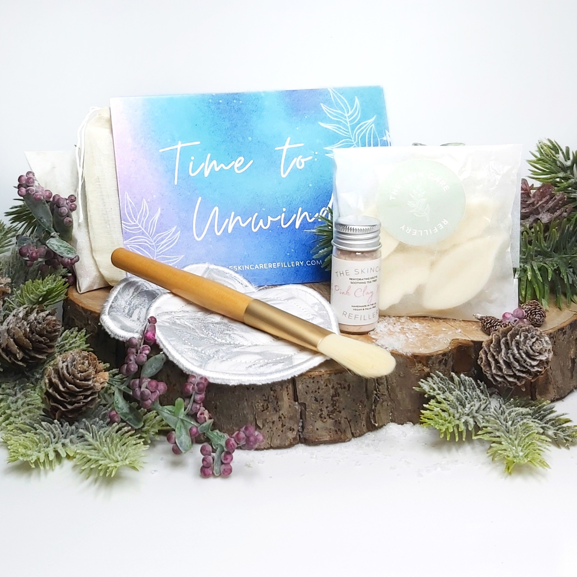 Items from The Skincare Refillery Letterbox Gift Set on a log slice with Christmas  foliage. Natural Beauty Christmas Gift Guide by Beauty Folio