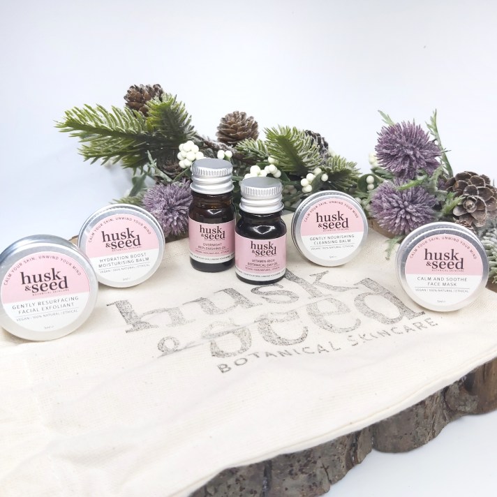 Husk & Seed Skincare Facial Collection Sample Set miniature bottles and tins sat on the linen bag with Christmas foliage. Natural Beauty Christmas Gift Guide by Beauty Folio