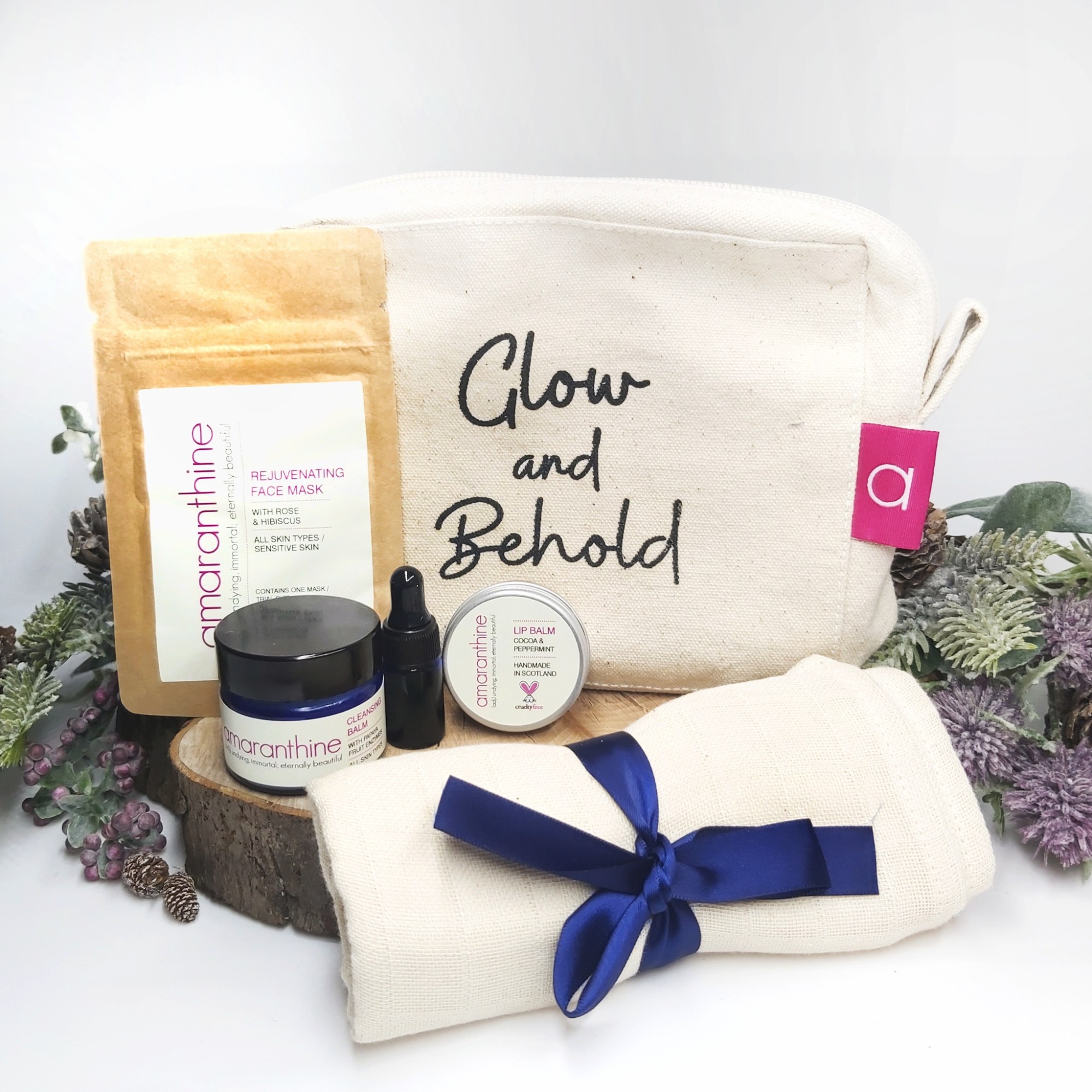 Amaranthine Skincare's Minis Bundle branded cosmetic bag and items on a log slice with festive foliage. Natural Beauty Christmas Gift Guide by Beauty Folio.