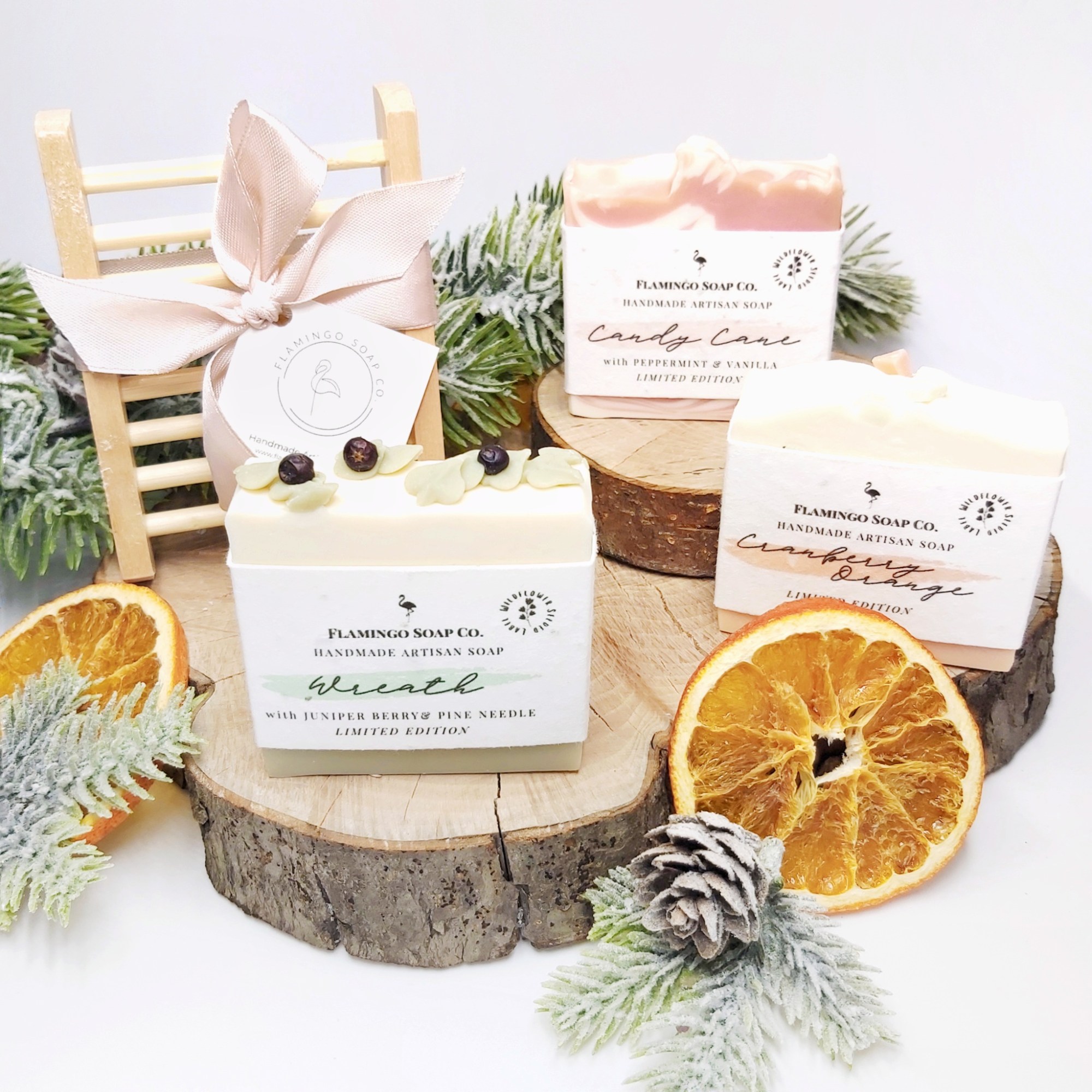 3 soap bars sat on log slices with a wooden soap tray standing ion the background. Oranges slices and christmas foliage around the edges. Natural Beauty Christmas Gift Guide by Beauty Folio