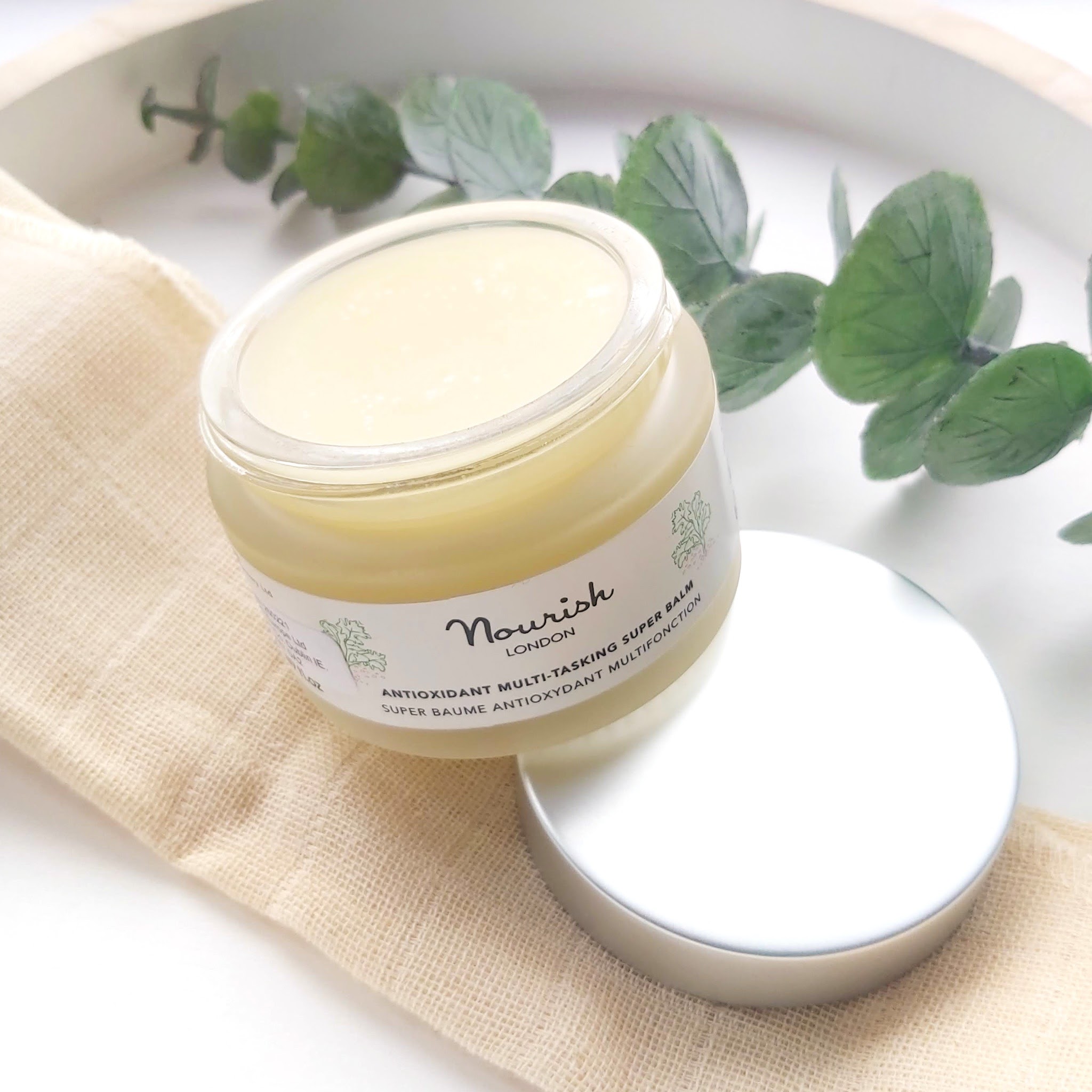 Nourish London Antioxidant Multi-Tasking Super Balm with muslin cloth with Eucalyptus foliage on a white and wood tray - Review by Beauty Folio