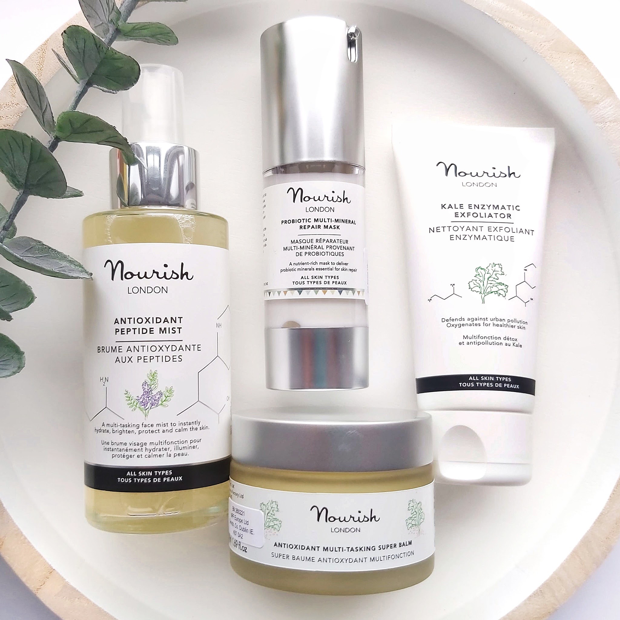 Nourish London Organic, Vegan, Natural and Cruelty Free Multipurpose Skincare products with Eucalyptus foliage on a white and wood tray - Review by Beauty Folio