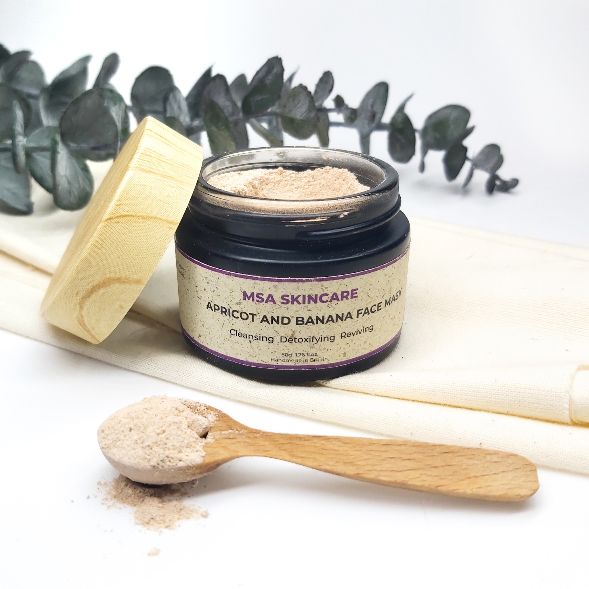 An open jar of MSA Skincare face mask with a white background, sitting on top of linen fabric with a stem of eucalyptus stem in the background. Natural skincare review by Beauty Folio