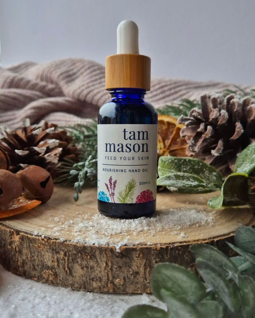 Tam Mason Nourishing Hand and Nail Oil on a log slice with foliage and artificial snow - Photo by Beauty Folio, Green Beauty Content Creator