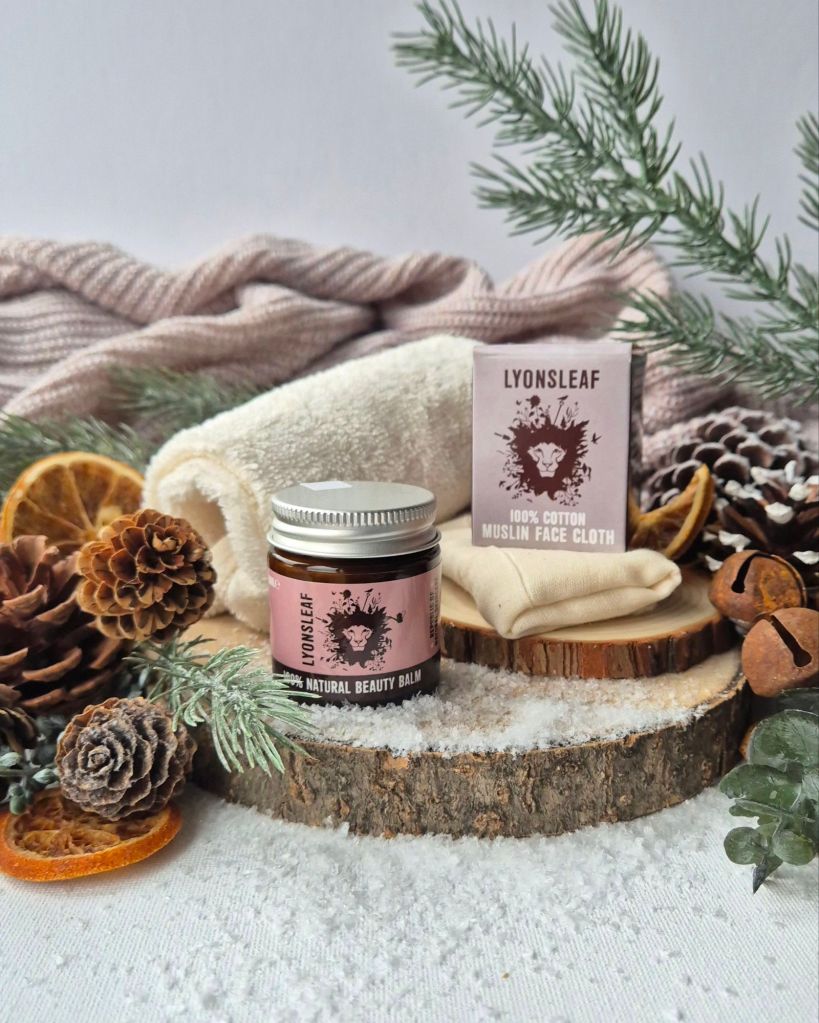 Lyonsleaf Beauty Balm and cloths on a log slice with foliage and artificial snow - Photo by Beauty Folio, Green Beauty Content Creator