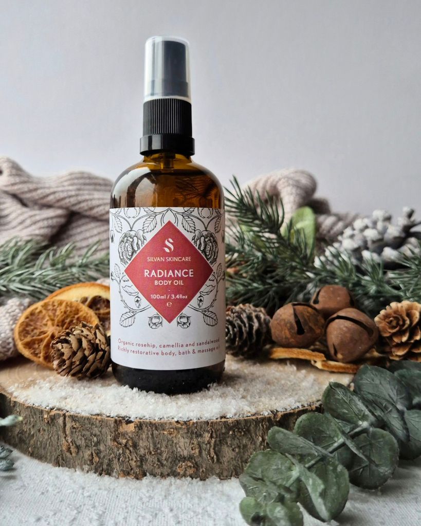 Silvan Skincare Radiance Body Oil on a log slice with foliage and artificial snow - Photo by Beauty Folio, Green Beauty Content Creator