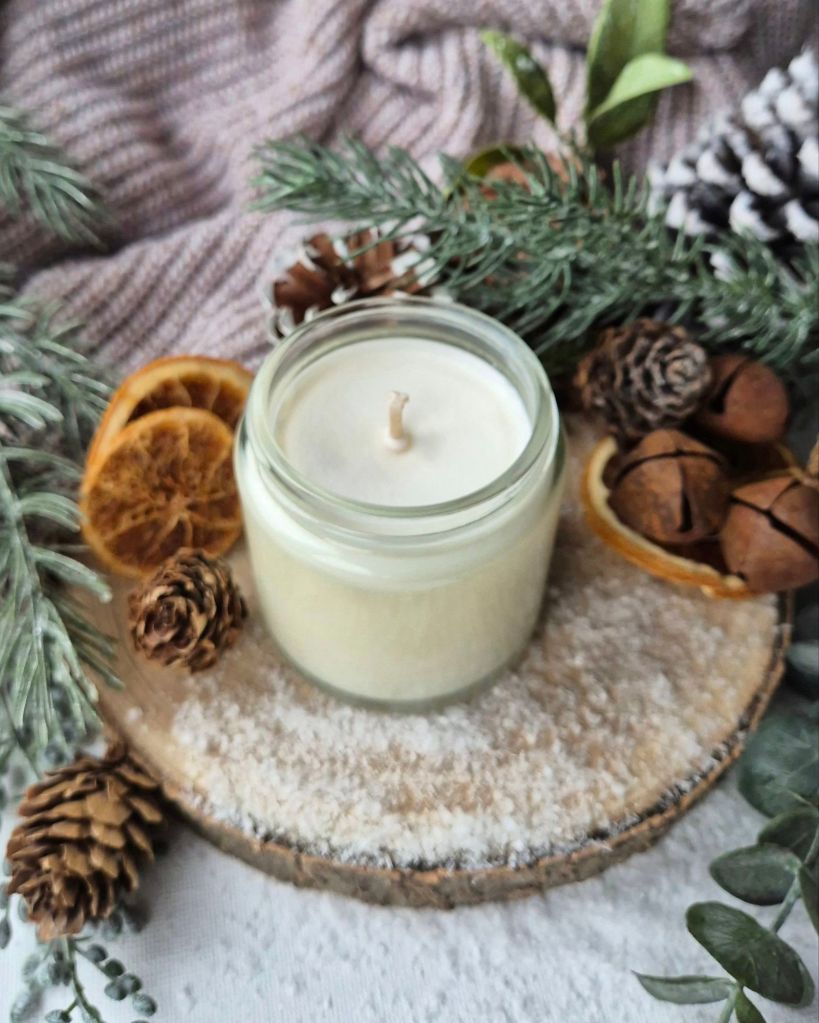 Acala's Jasmine Candle in a glass jar on a log slice with foliage and artificial snow - Photo by Beauty Folio, Green Beauty Content Creator
