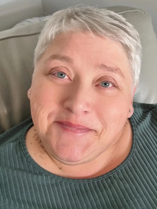 Julie is sat against a grey leather chair and is wearing a green ribbed top. She is gently smiling at the camera.